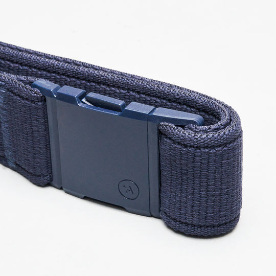 A close-up of the Atlas elastic stretch belt by Arcade Belts in navy blue, featuring a rectangular plastic buckle with a small circular symbol and a textured, woven look, shown against a white background.