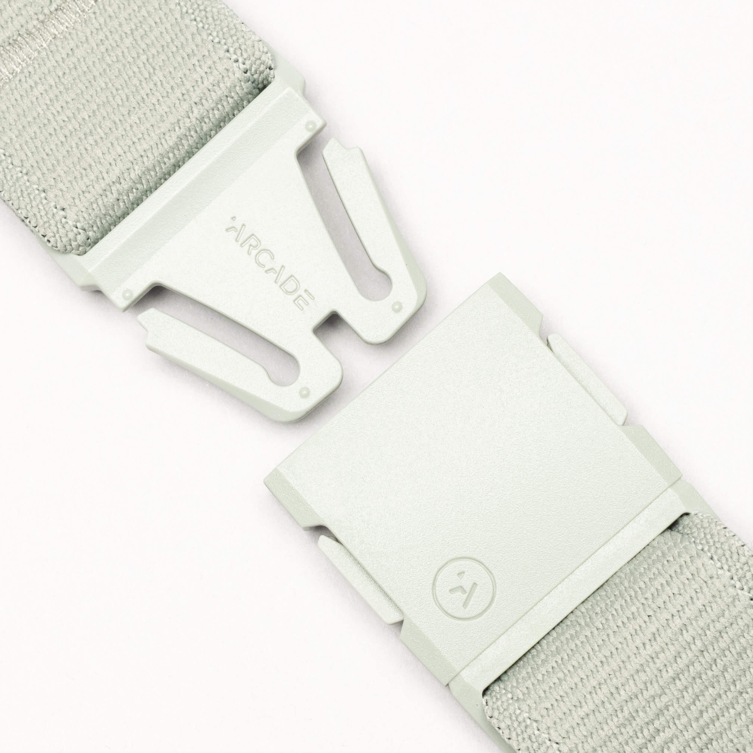 Close-up of a light gray Arcade Belts Atlas adventure belt with a partially unclasped A2 buckle. "ARCADE" is on one side of the buckle and a smiley face symbol is on the other.