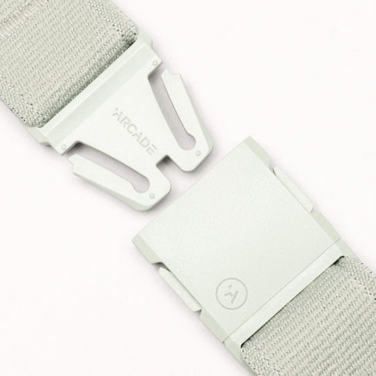 Close-up of a light gray Arcade Belts Atlas adventure belt with a partially unclasped A2 buckle. "ARCADE" is on one side of the buckle and a smiley face symbol is on the other.