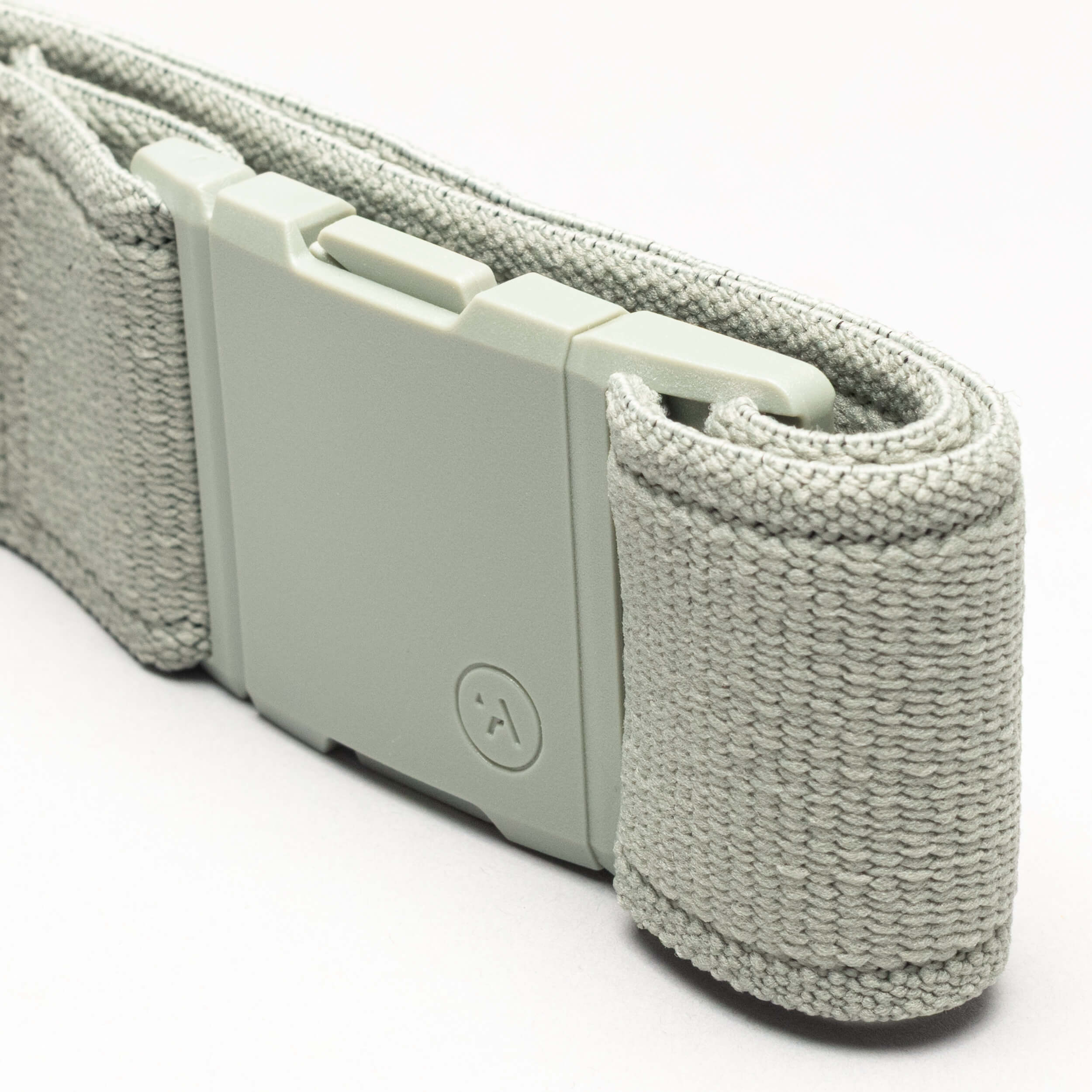 A close-up of the Atlas by Arcade Belts—a light gray, performance stretch strap with an A2 buckle and textured woven material—coiled neatly on a light background, perfect for adventure belt enthusiasts.