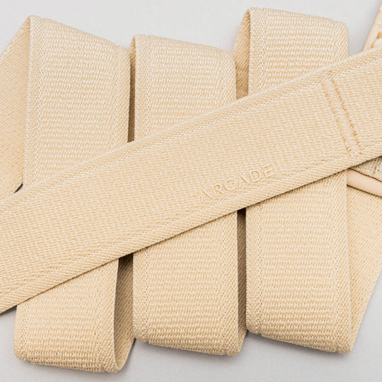 A close-up of beige woven fabric straps in a crisscross pattern features ARCADE embossed on the center, highlighting the Atlas elastic stretch belt by Arcade Belts—an ideal choice for travel.