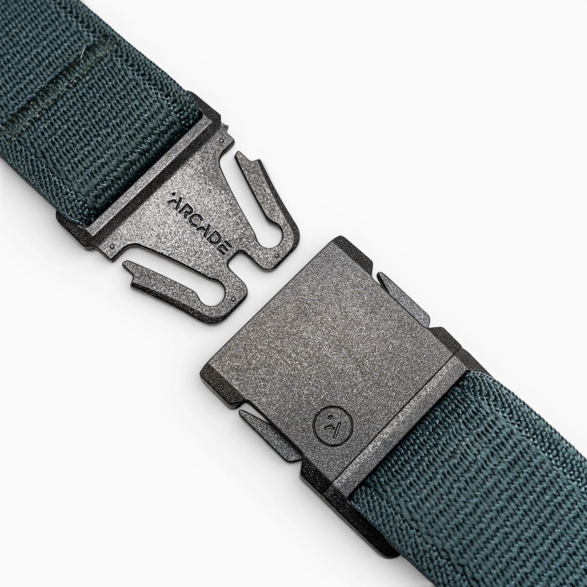 A close-up of the green Atlas travel belt by Arcade Belts, showing a black metal buckle engraved with ARCADE and featuring a two-prong locking mechanism. The belt is partially unfastened.
