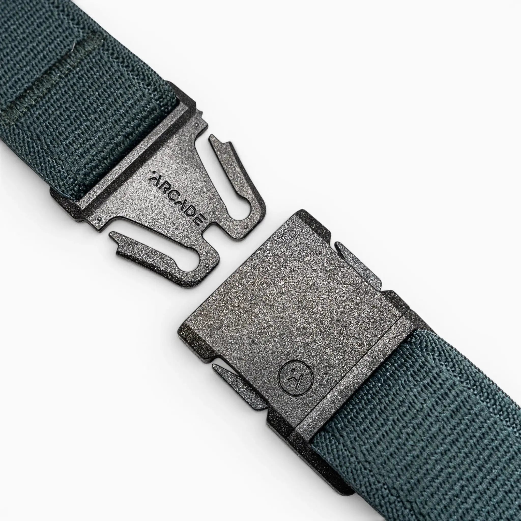 A close-up of the green Atlas travel belt by Arcade Belts, showing a black metal buckle engraved with ARCADE and featuring a two-prong locking mechanism. The belt is partially unfastened.
