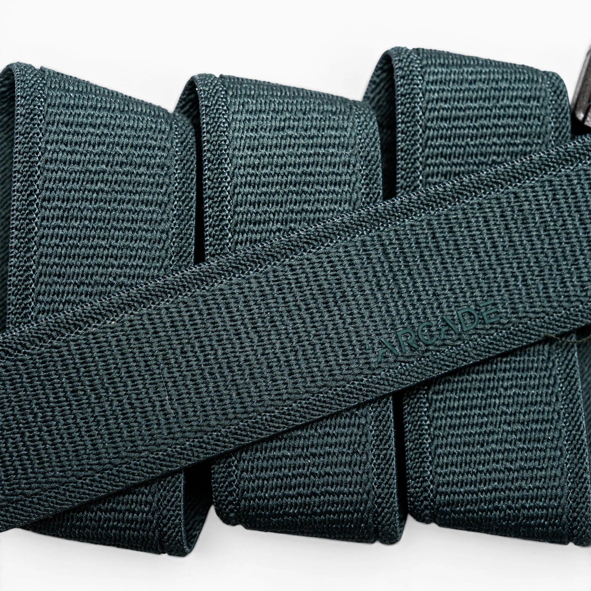 A close-up of a folded dark green Atlas elastic stretch belt by Arcade Belts, featuring a woven texture and the brand name subtly embossed at the center.