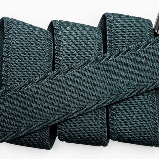 A close-up of a folded dark green Atlas elastic stretch belt by Arcade Belts, featuring a woven texture and the brand name subtly embossed at the center.