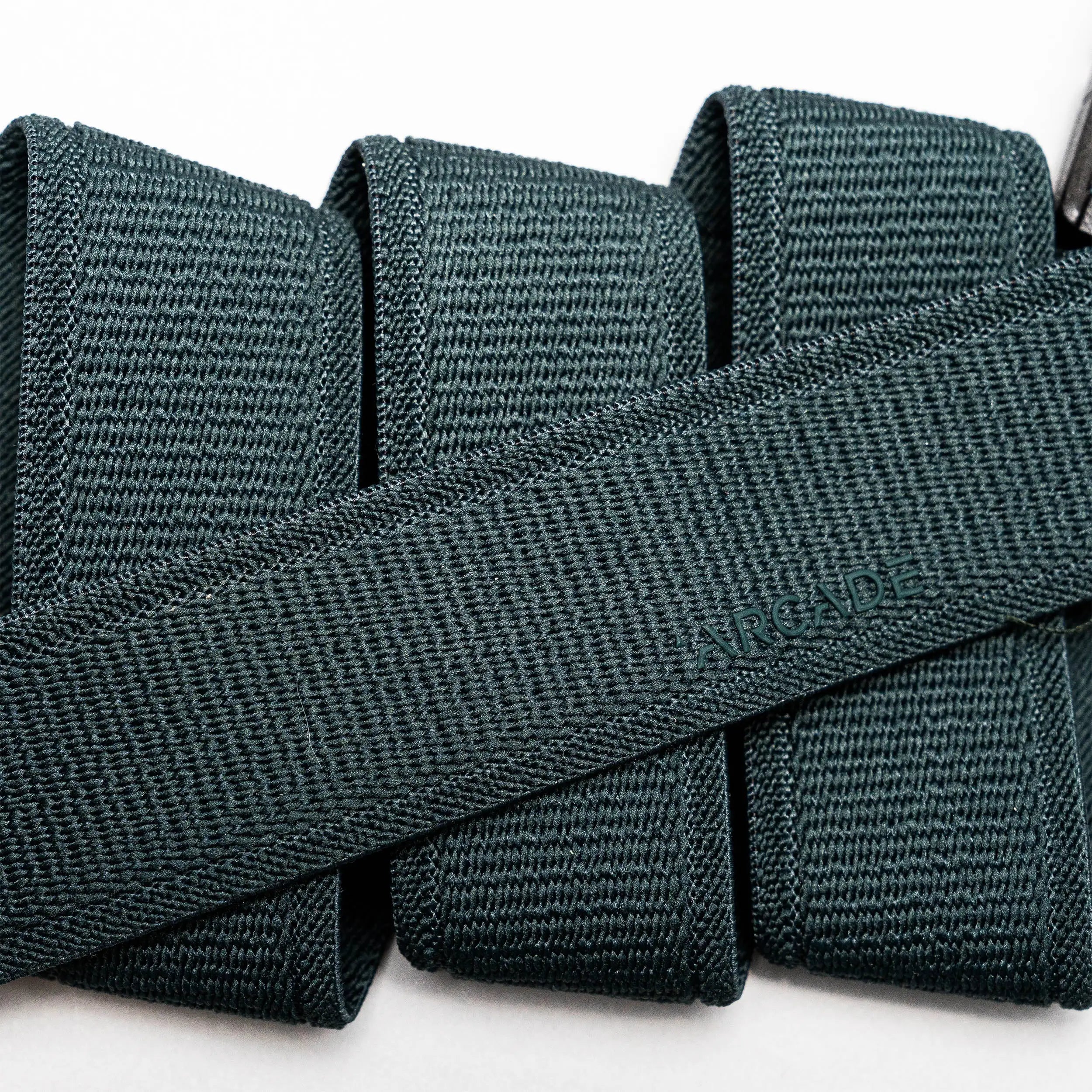 A close-up of a folded dark green Atlas elastic stretch belt by Arcade Belts, featuring a woven texture and the brand name subtly embossed at the center.