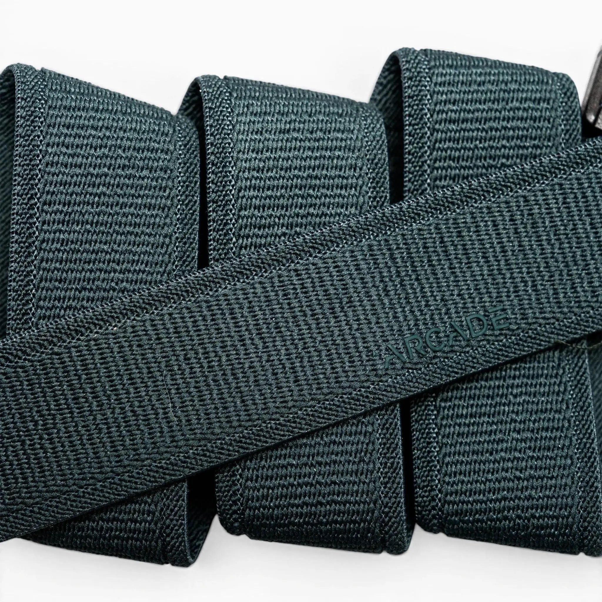 A close-up of a folded dark green Atlas elastic stretch belt by Arcade Belts, featuring a woven texture and the brand name subtly embossed at the center.