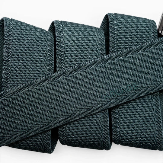 A close-up of a folded dark green Atlas elastic stretch belt by Arcade Belts, featuring a woven texture and the brand name subtly embossed at the center.