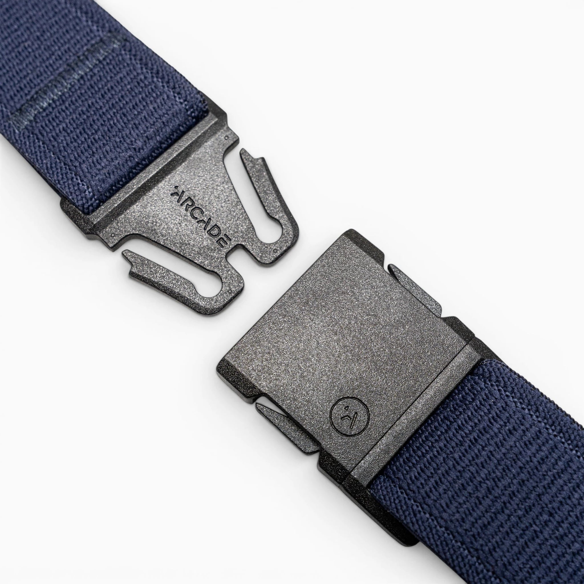 A close-up of a black plastic buckle with Arcade Belts branding on one side, attached to the navy blue Atlas elastic stretch belt, shown unbuckled against a light gray background.