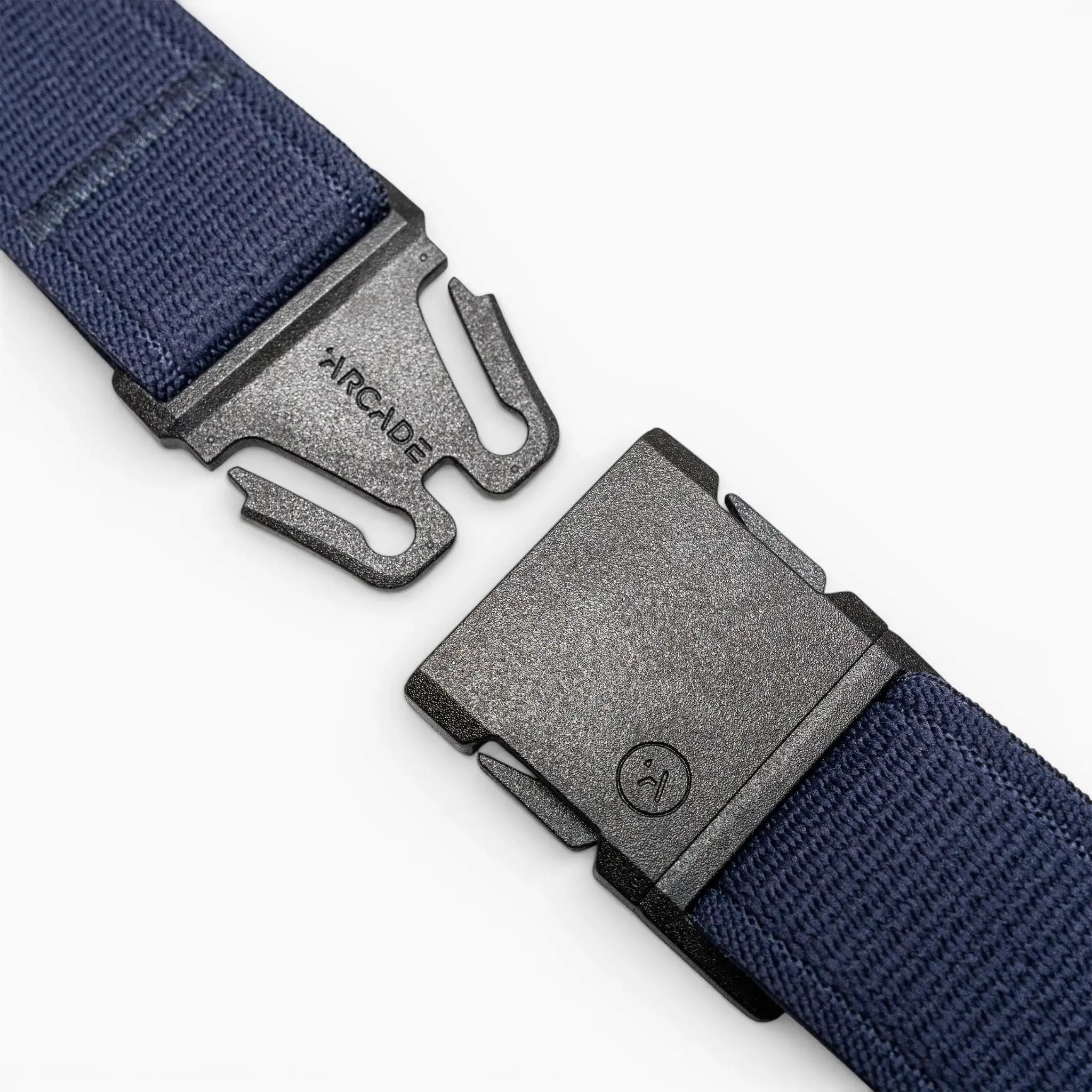 A close-up of a black plastic buckle with Arcade Belts branding on one side, attached to the navy blue Atlas elastic stretch belt, shown unbuckled against a light gray background.