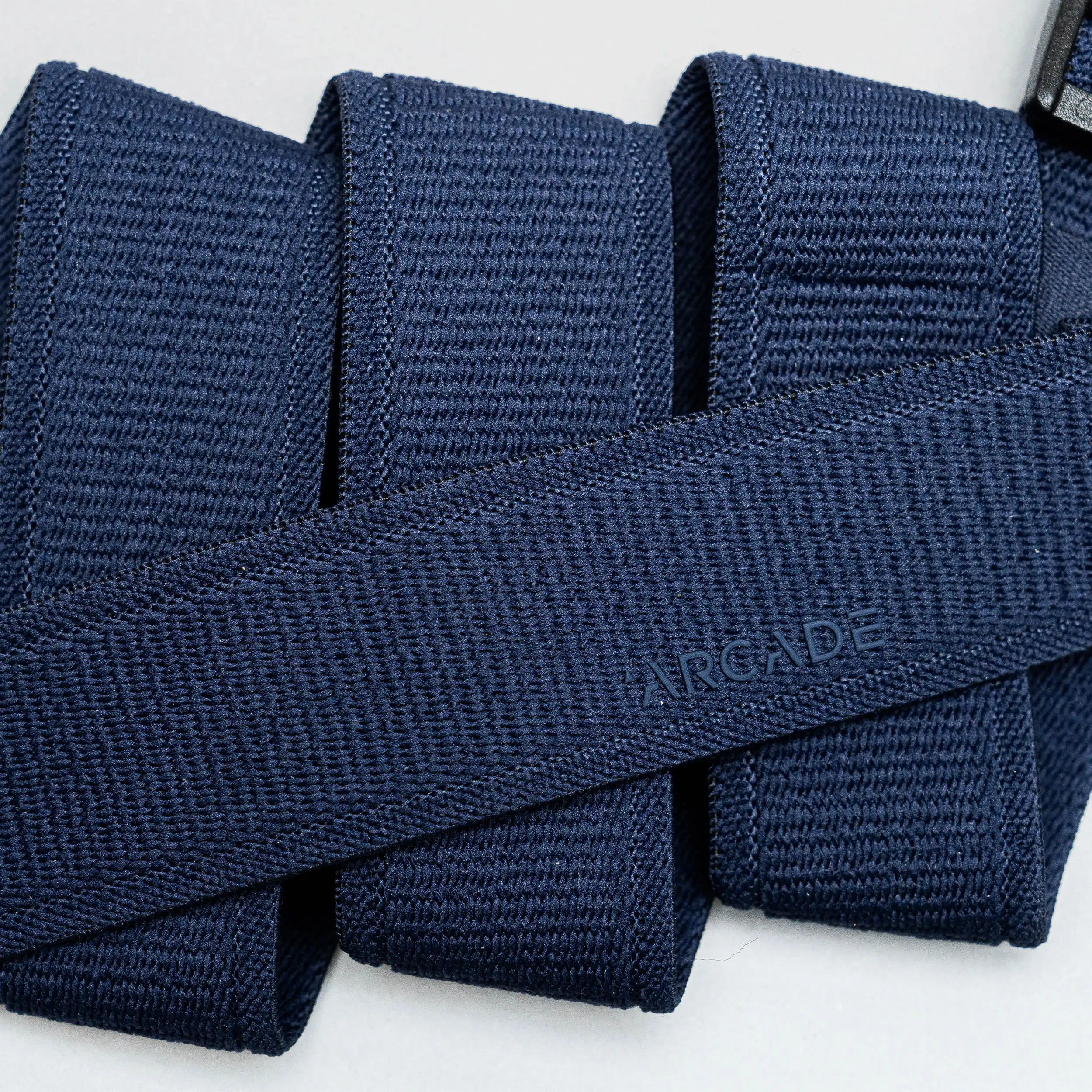 A close-up of the Atlas belt by Arcade Belts in navy blue woven fabric, neatly folded with ARCADE subtly embossed, highlights its Elastic Stretch Belt design for superior comfort and flexibility.