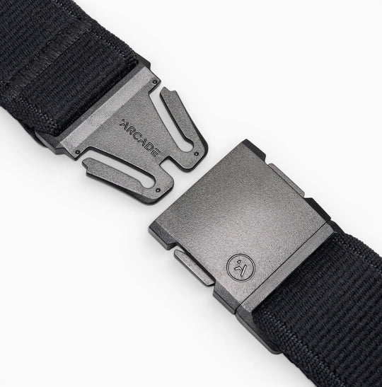 Close-up of the Atlas belt by Arcade Belts, a black elastic stretch belt with a metal quick-release buckle—partially unclasped, ARCADE engraved on one side. White background.