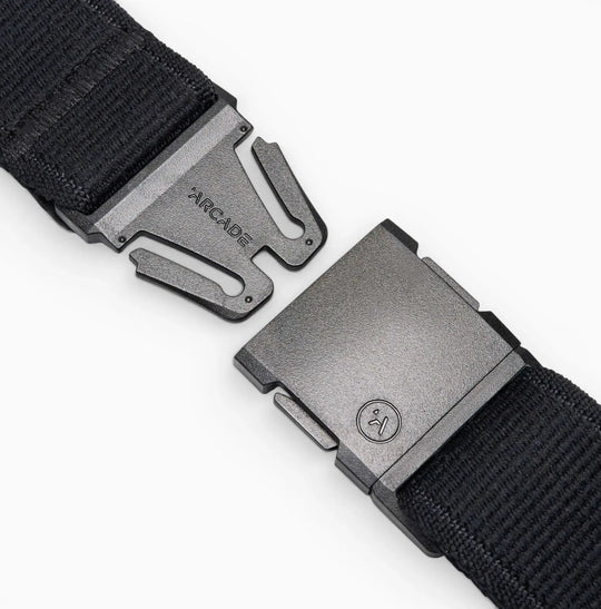 Close-up of the Atlas belt by Arcade Belts, a black elastic stretch belt with a metal quick-release buckle—partially unclasped, ARCADE engraved on one side. White background.