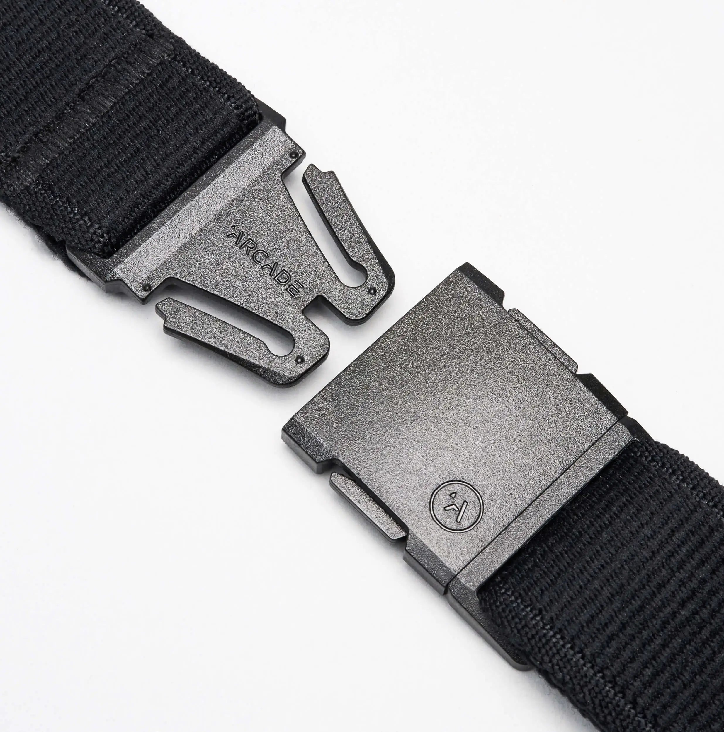 A close-up of the Atlas travel belt by Arcade Belts in black fabric, featuring a metal buckle—partially unclasped—with ARCADE engraved on one side and a logo on the other, set against a white background.
