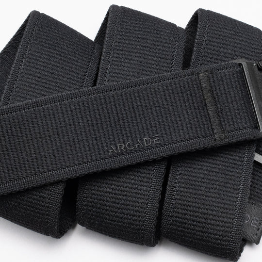 A close-up of the Atlas belt by Arcade Belts, featuring a black low-profile design with a textured surface and a subtle Arcade logo. Coiled with part of its plastic buckle visible—perfect for travel enthusiasts.