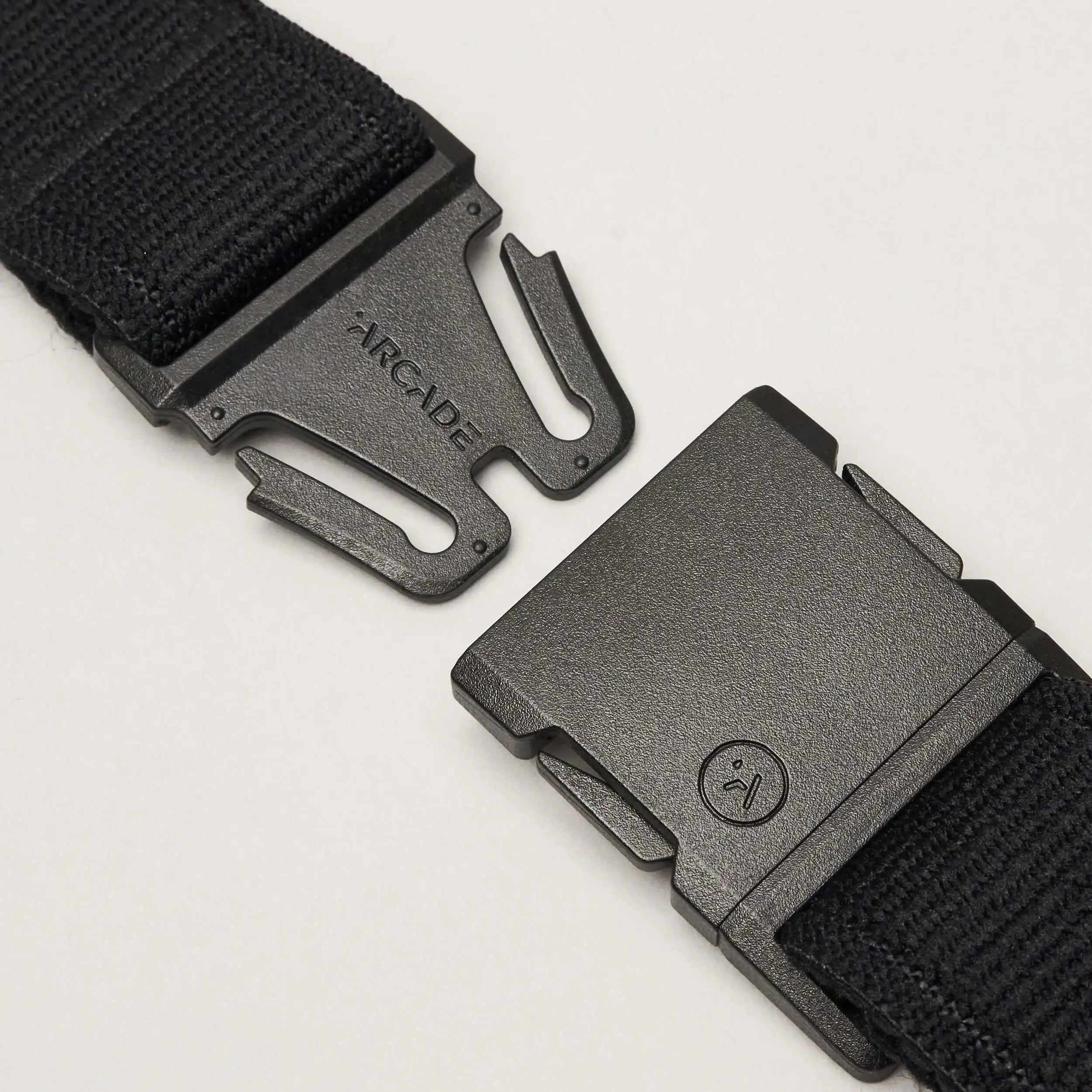 A close-up of the Atlas elastic stretch belt by Arcade Belts in black, featuring a plastic quick-release buckle. The unfastened low-profile buckle shows the Arcade Belts brand name on one side and a small circular face logo on the other.