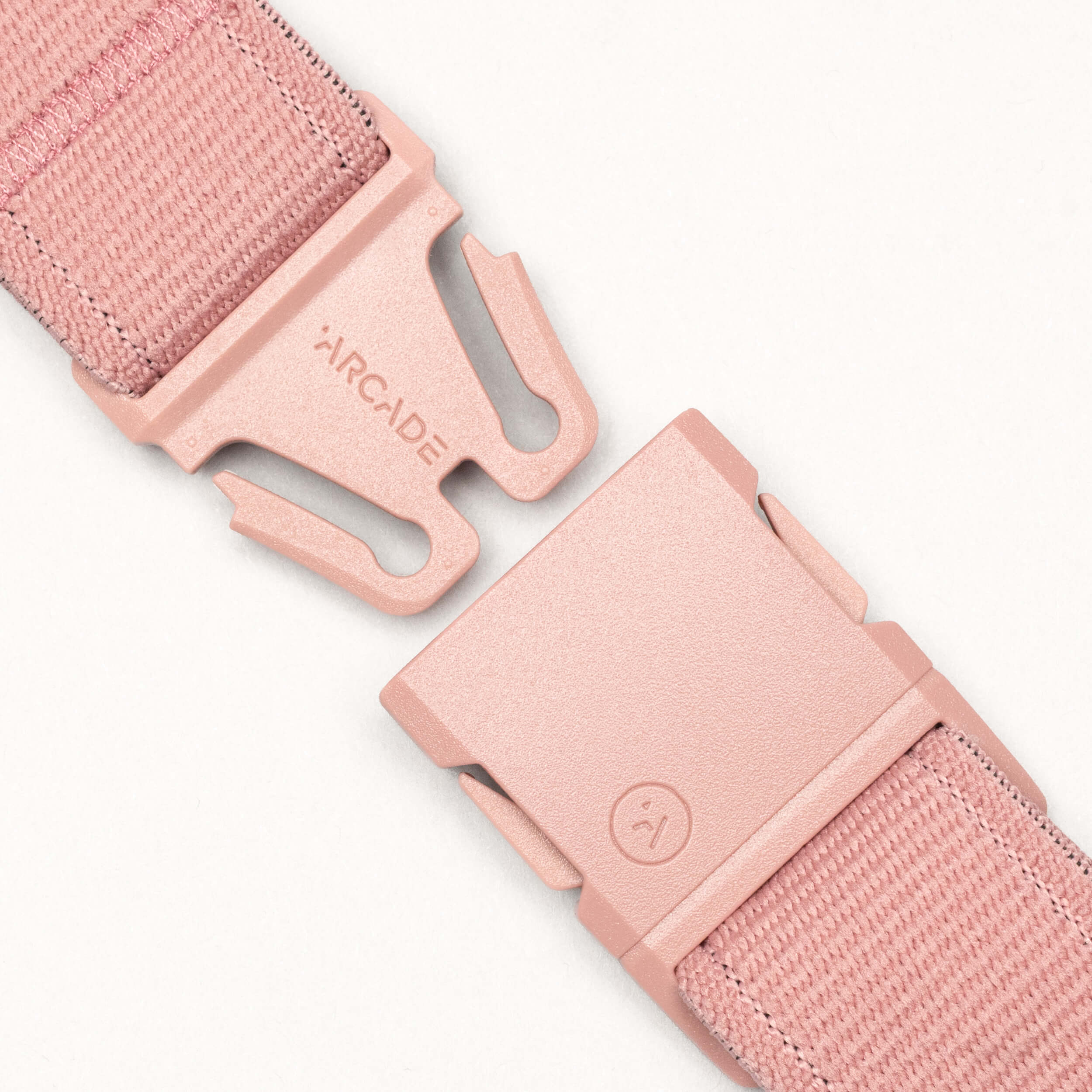 Close-up of the Arcade Belts Atlas adventure belt in pink, featuring a matching pink plastic A2 buckle—partially unclasped—with "ARCADE" printed on one side. The background is a plain light color.