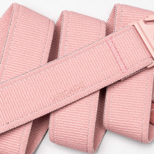 A close-up of the Atlas performance stretch belt by Arcade Belts, featuring a matching pink A2 buckle and the word ARCADE subtly embossed on the neatly folded light pink strap.
