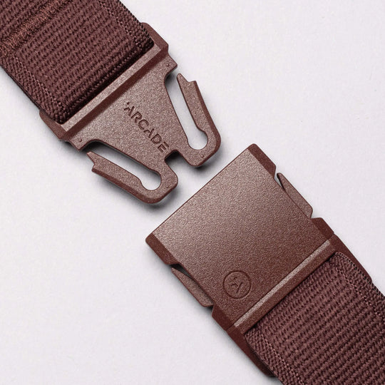 Close-up of a brown Atlas belt by Arcade Belts with a plastic buckle, separated at the clasp. “ARCADE” appears on one side of the buckle, shown against a light solid background.