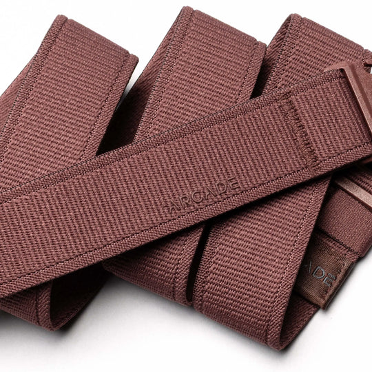 A close-up of the Atlas maroon stretch webbing belt by Arcade Belts, featuring a textured pattern and a partially visible plastic buckle—perfect for travel belt enthusiasts. ARCADE is embossed on the belt.