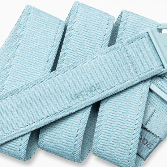 A close-up of the Atlas adventure belt by Arcade Belts in light blue, featuring a plastic A2 buckle. The word “ARCADE” is embossed on the belt’s fabric. This performance stretch belt is coiled and layered over itself.