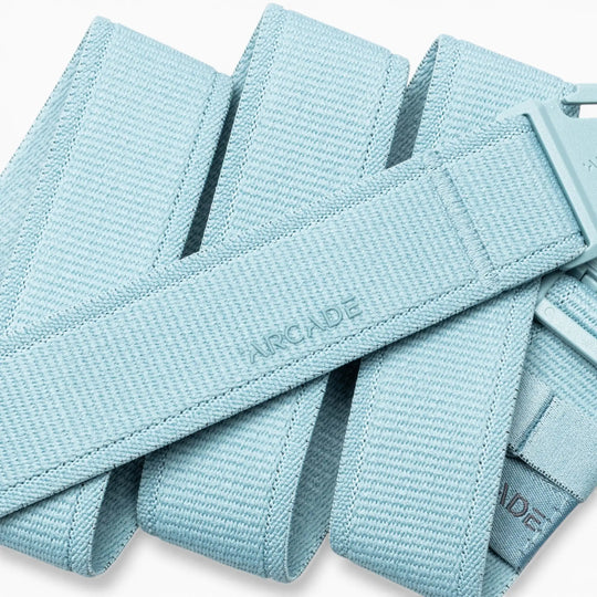 A close-up of the Atlas adventure belt by Arcade Belts in light blue, featuring a plastic A2 buckle. The word “ARCADE” is embossed on the belt’s fabric. This performance stretch belt is coiled and layered over itself.