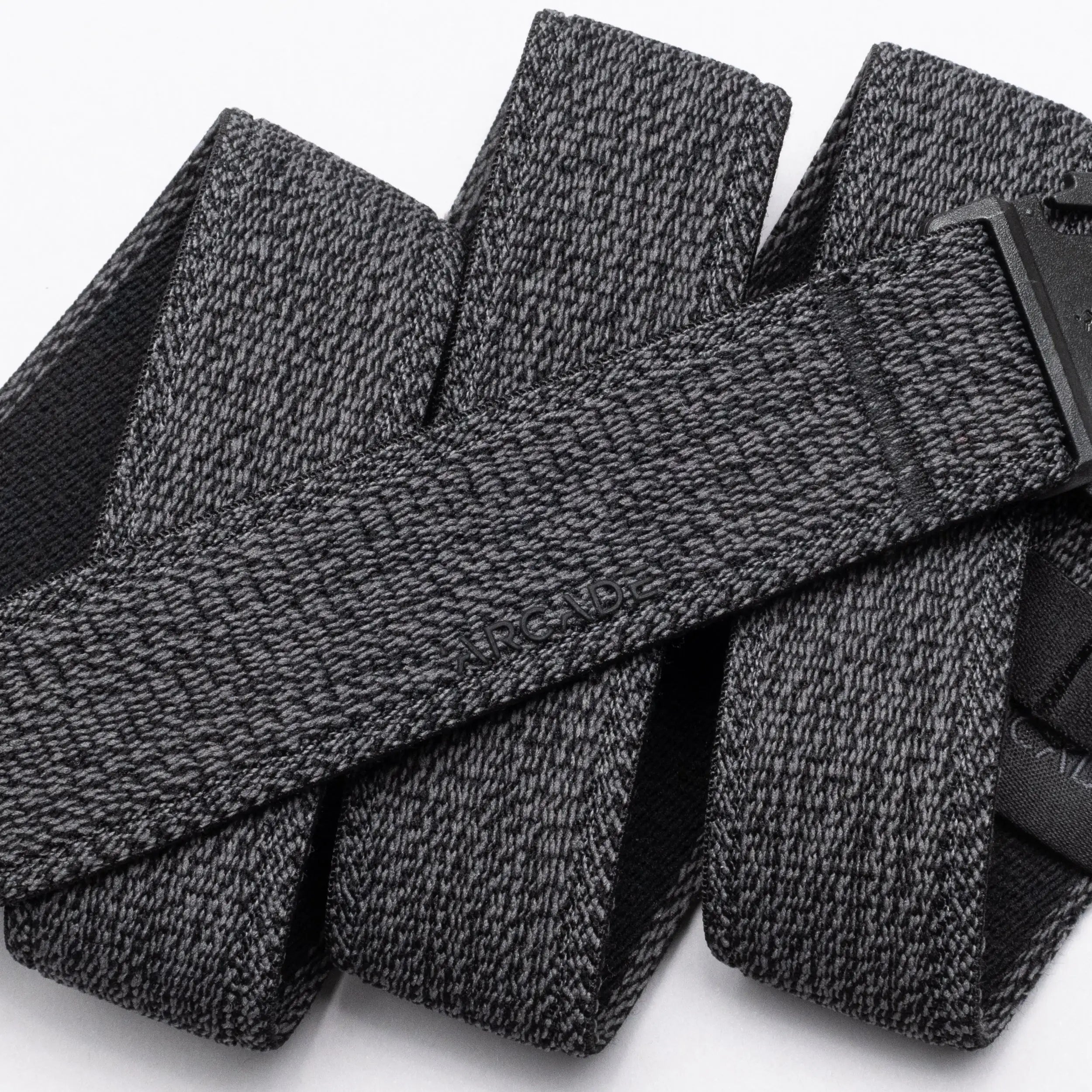 A close-up of the Atlas belt by Arcade Belts showcases its textured gray stretch webbing and black buckle. The elastic belt, looped on a white background, features the ARCADE branding subtly embossed on its surface.