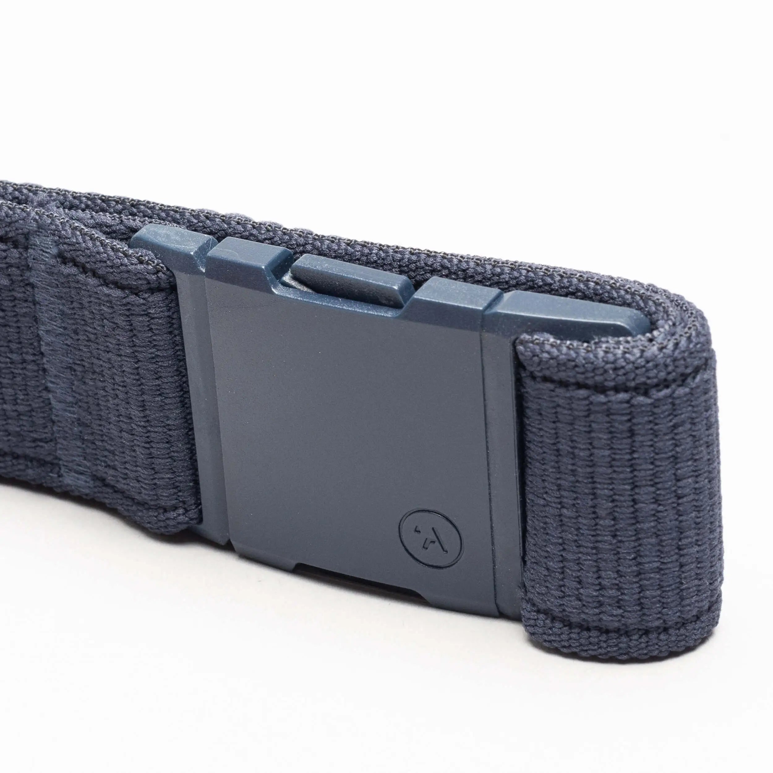 A close-up of the Atlas belt by Arcade Belts in navy blue stretch webbing, featuring a rectangular matte-finish plastic buckle with a small circular logo. The low-profile belt is displayed on a white surface.
