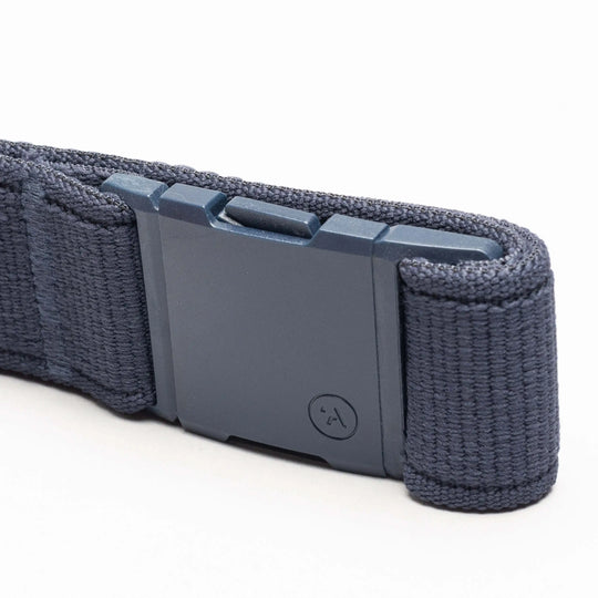 A close-up of the Atlas belt by Arcade Belts in navy blue stretch webbing, featuring a rectangular matte-finish plastic buckle with a small circular logo. The low-profile belt is displayed on a white surface.