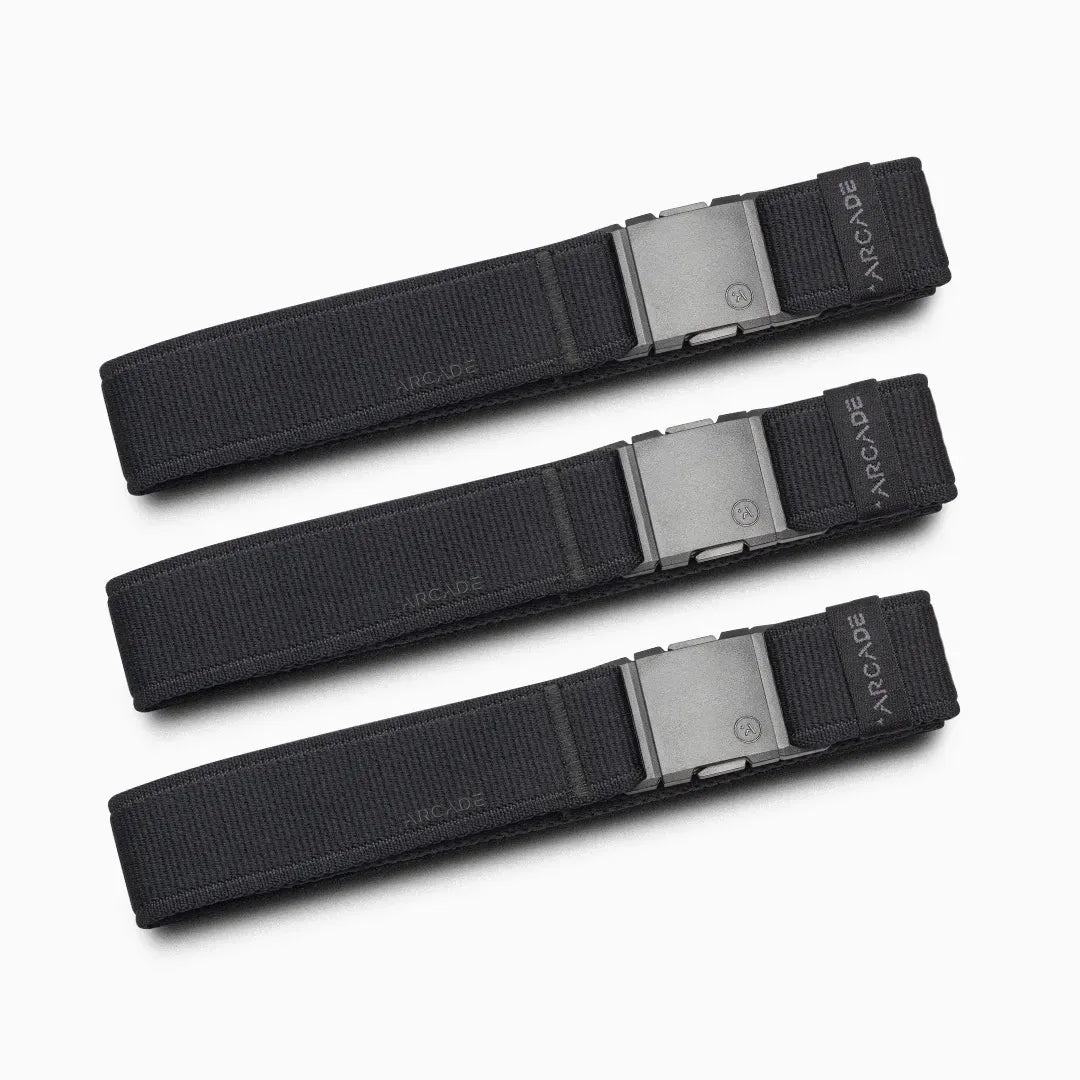 Three identical Atlas Gifting Kit black fabric belts from Arcade Belts, each with a rectangular metal buckle, are arranged parallel to each other on a light gray background. Designed with performance stretch for all-day comfort, the word ARCADE is visible on each belt near the buckle.