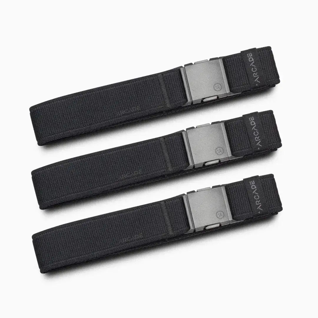 Three identical Atlas Gifting Kit black fabric belts from Arcade Belts, each with a rectangular metal buckle, are arranged parallel to each other on a light gray background. Designed with performance stretch for all-day comfort, the word ARCADE is visible on each belt near the buckle.
