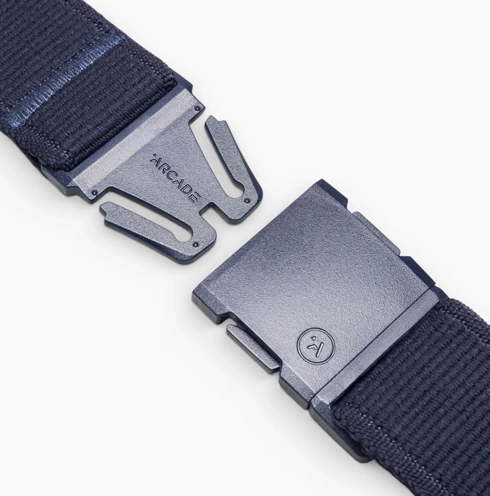 Close-up of the Atlas Elastic Stretch Belt by Arcade Belts in dark blue, featuring a metal buckle engraved with ARCADE. The partially unclasped buckle reveals the interlocking mechanism, emphasizing the belts stylish and functional travel-ready design.