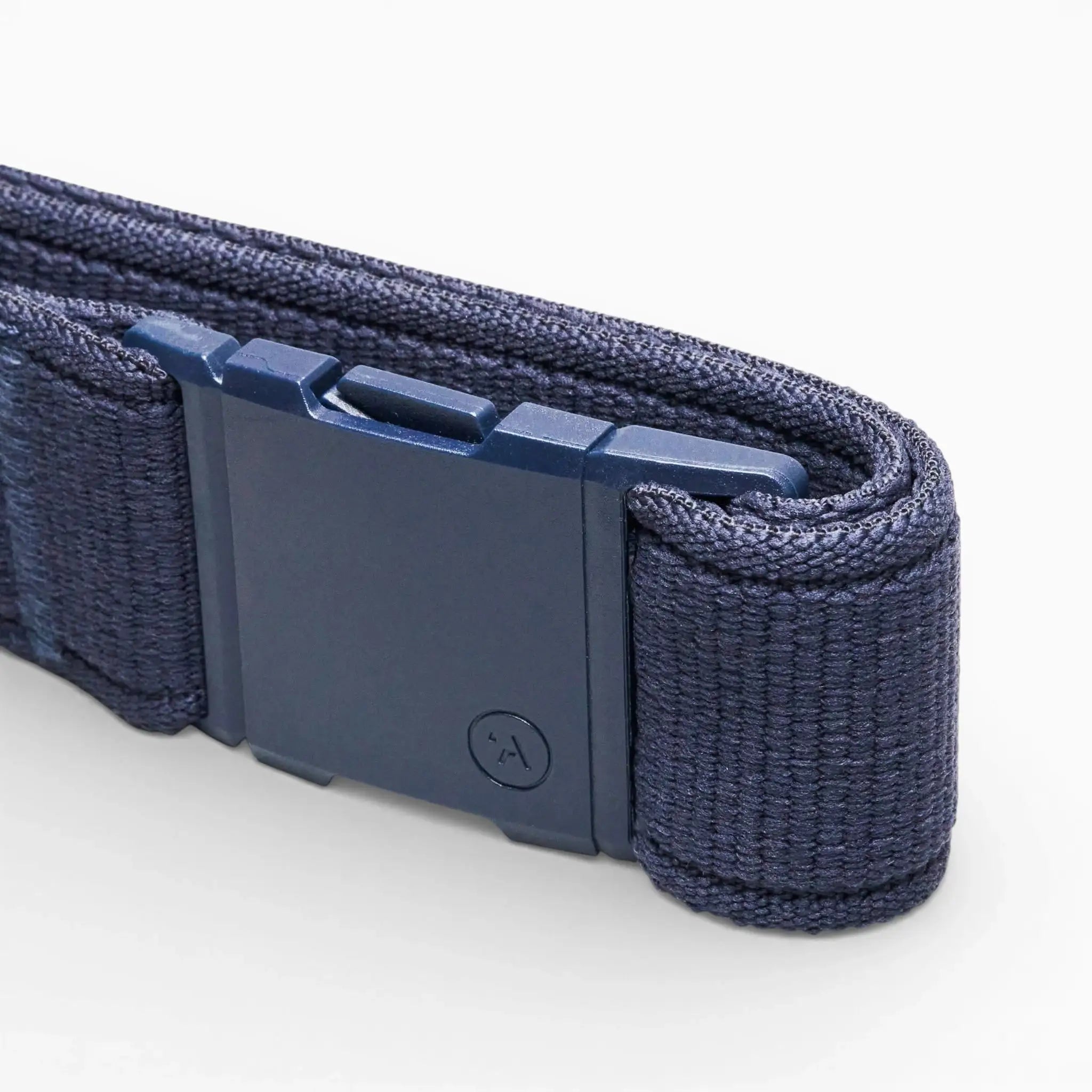 A close-up of the Atlas elastic stretch belt by Arcade Belts in navy blue, featuring a rectangular plastic buckle with a small circular symbol and a textured, woven look, shown against a white background.