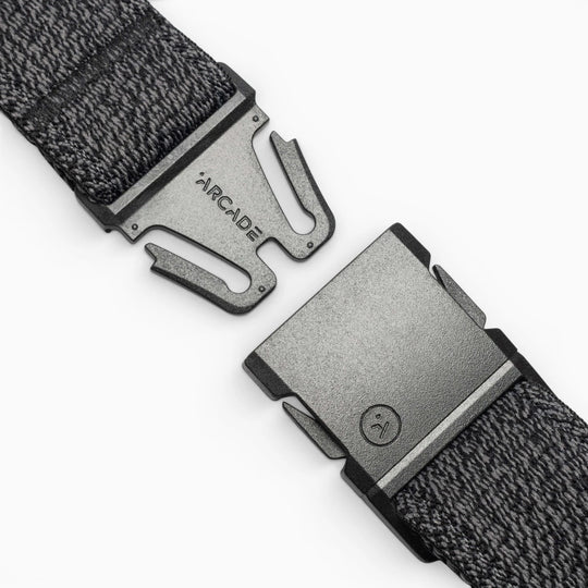 A close-up of the gray woven Atlas belt by Arcade Belts, featuring a black buckle engraved with ARCADE. The partially unclasped buckle uses a simple, secure fastening mechanism—ideal for travel.