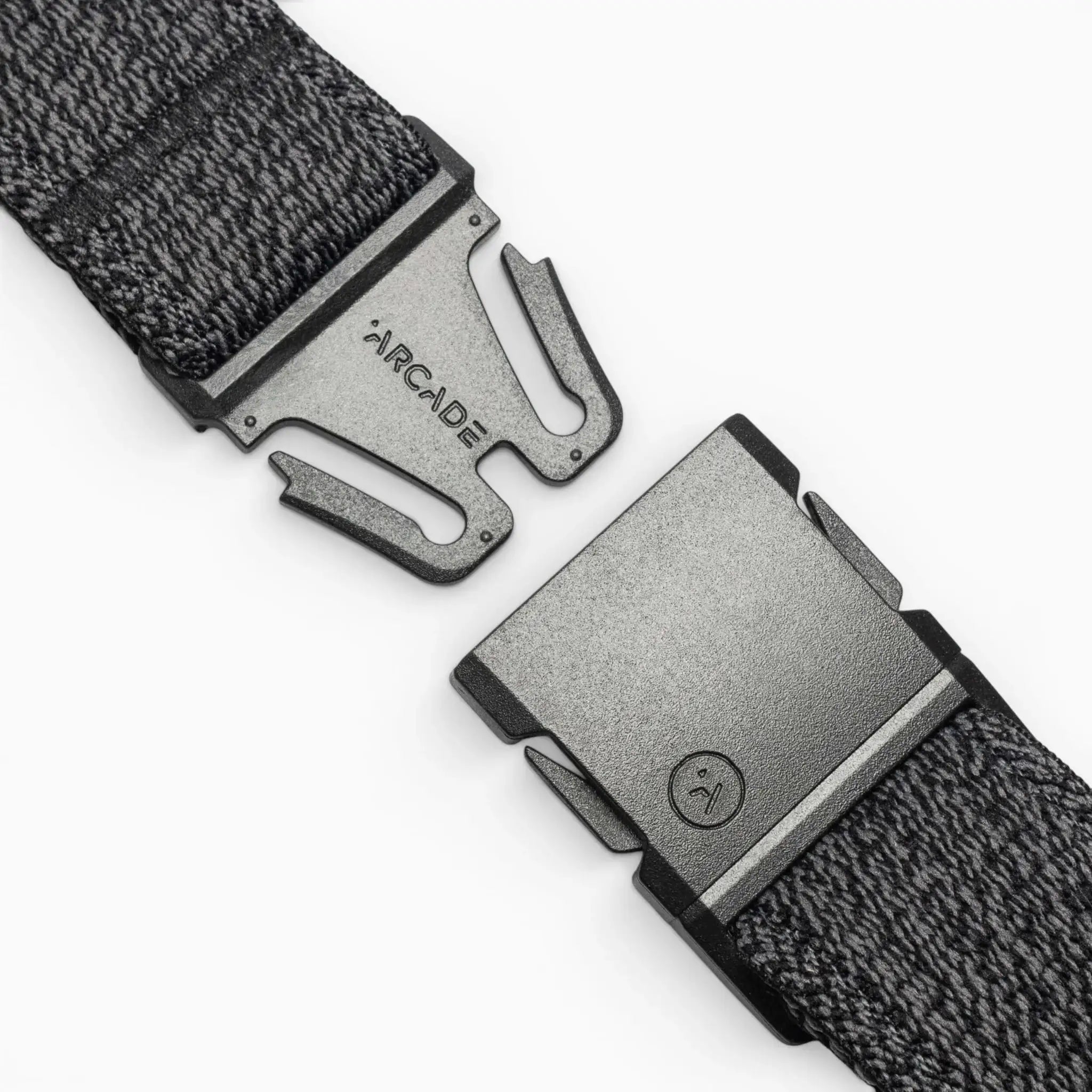 A close-up of the gray woven Atlas belt by Arcade Belts, featuring a black buckle engraved with ARCADE. The partially unclasped buckle uses a simple, secure fastening mechanism—ideal for travel.