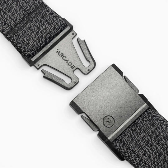 A close-up of the gray woven Atlas belt by Arcade Belts, featuring a black buckle engraved with ARCADE. The partially unclasped buckle uses a simple, secure fastening mechanism—ideal for travel.