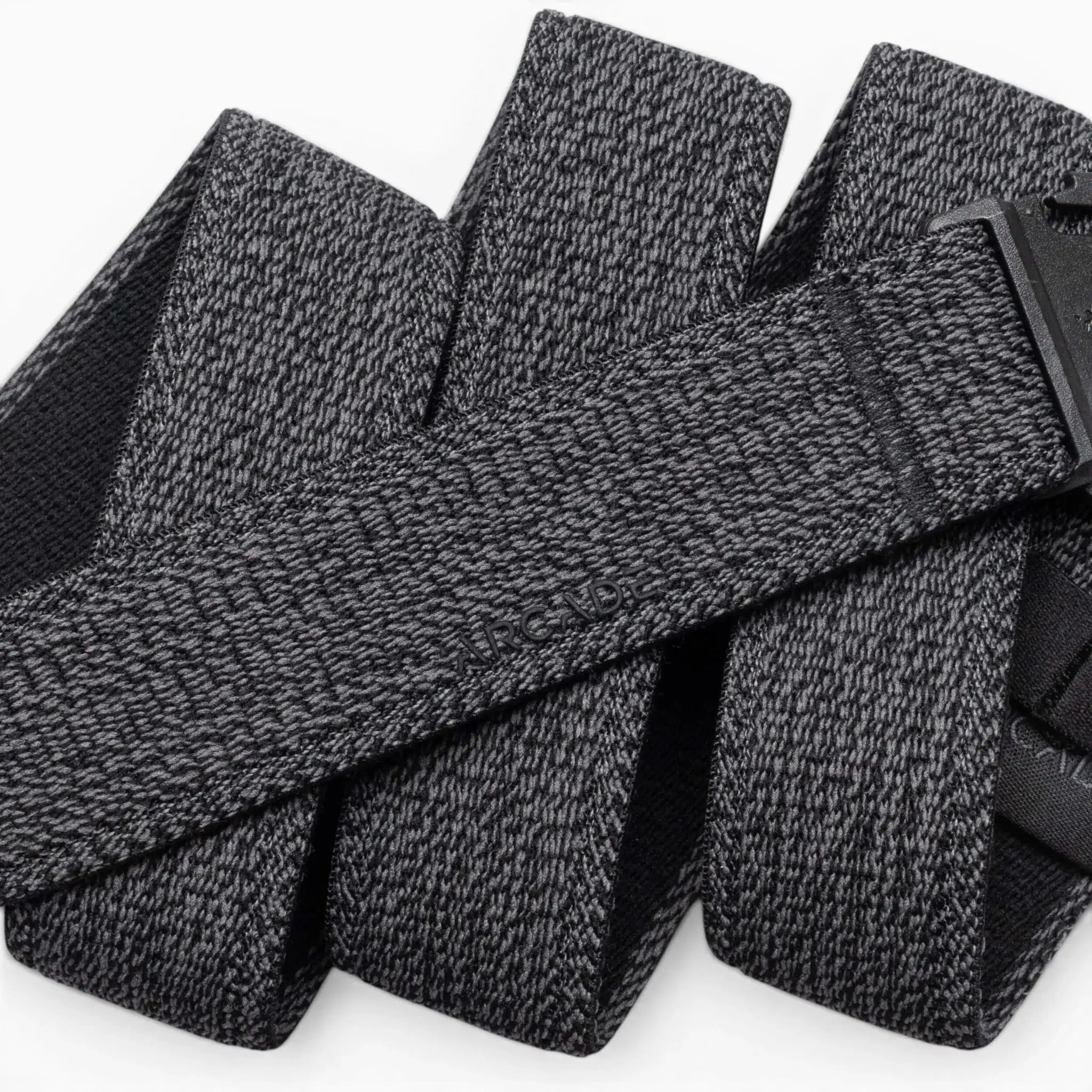 A close-up of the Atlas belt by Arcade Belts showcases its textured gray stretch webbing and black buckle. The elastic belt, looped on a white background, features the ARCADE branding subtly embossed on its surface.