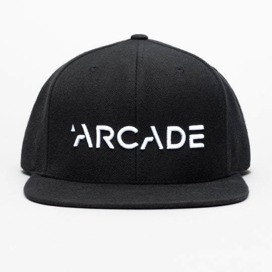 The Arcade Structured Hat by Arcade Belts is a black snapback cap with ARCADE boldly embroidered in white on the front and a sturdy plastic buckle, shown against a plain white background.