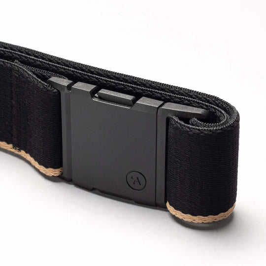 A close-up of the Arcade Belts Blackwood belt showcases its rectangular matte black A2 buckle and tan edge stitching, neatly rolled on a white surface.