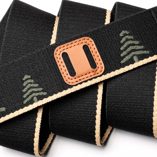 The Arcade Belts Blackwood features a black woven strap with tan edges, green tree patterns, and a brown leather accent with a rectangular cutout. It's shown loosely coiled on a white background.
