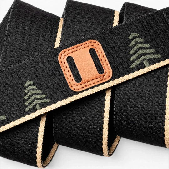 The Arcade Belts Blackwood features a black woven strap with tan edges, green tree patterns, and a brown leather accent with a rectangular cutout. It's shown loosely coiled on a white background.