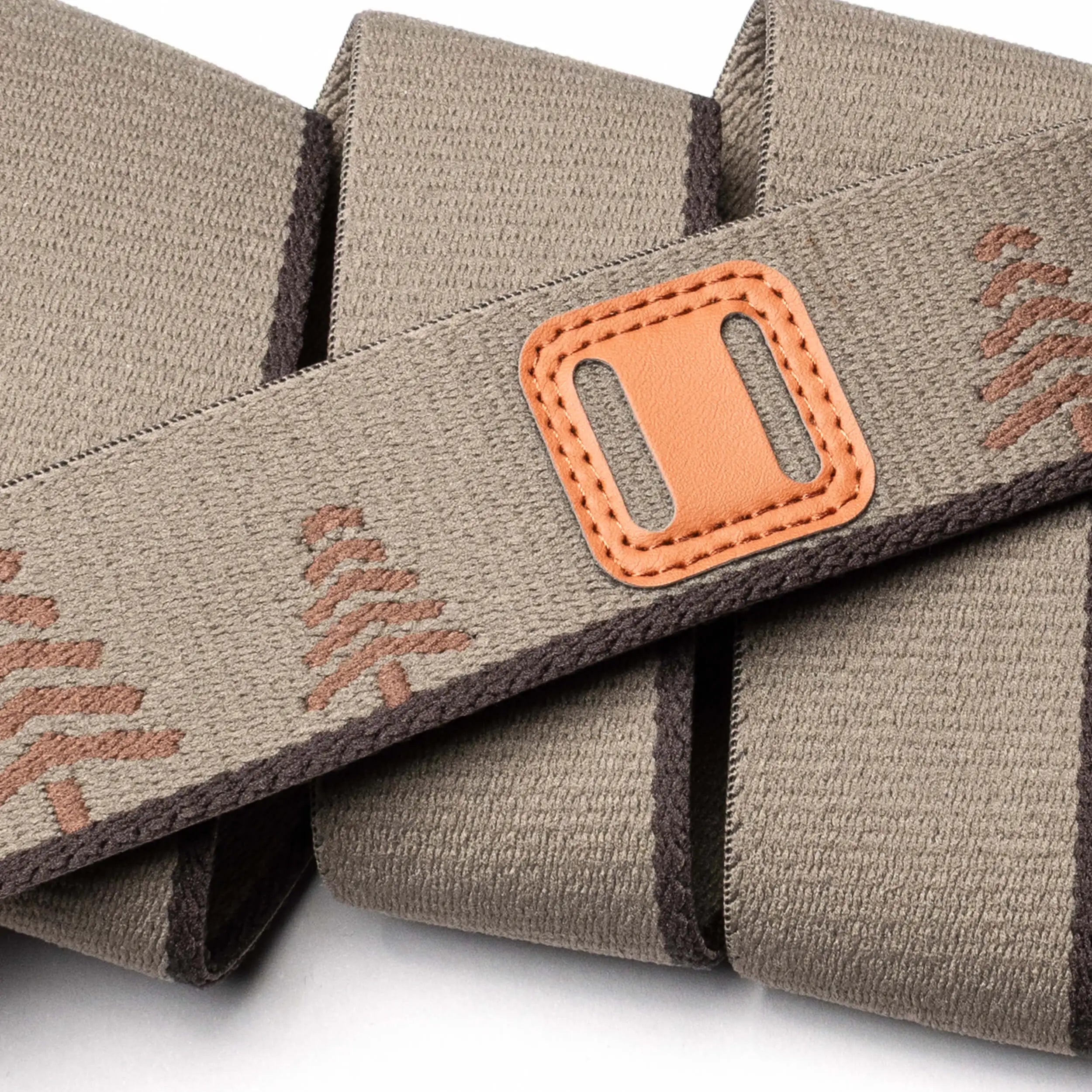 A close-up of the Arcade Belts Blackwood shows its beige fabric strap with brown stitching, decorative patterns, and a tan leather patch with a rectangular slot—highlighting the detailed craftsmanship in overlapping folds.
