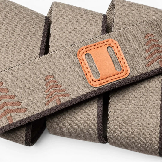 A close-up of the Arcade Belts Blackwood shows its beige fabric strap with brown stitching, decorative patterns, and a tan leather patch with a rectangular slot—highlighting the detailed craftsmanship in overlapping folds.