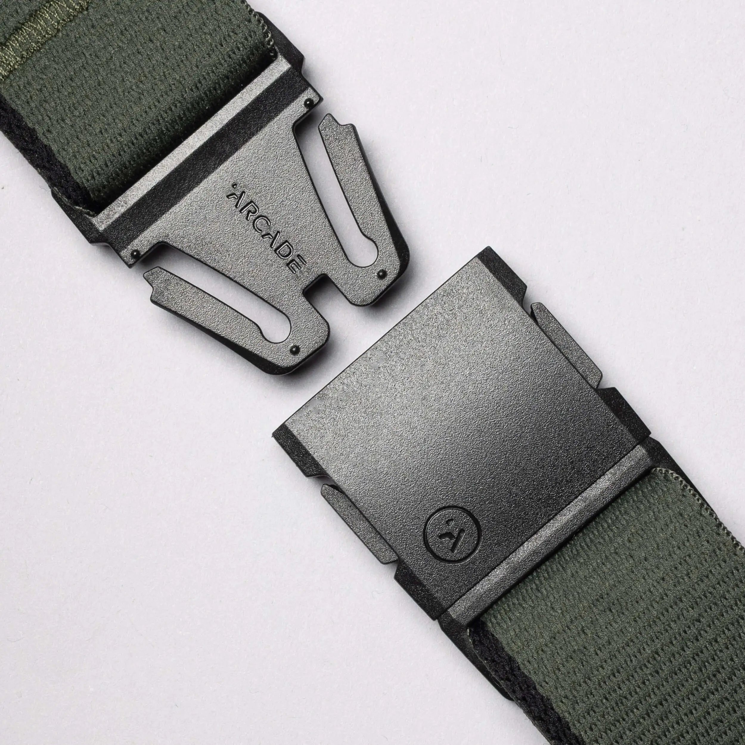A close-up of a green Arcade Belts Blackwood fabric belt with a black metal A2 buckle, partially unclasped to reveal ARCADE engraved on the clasp.