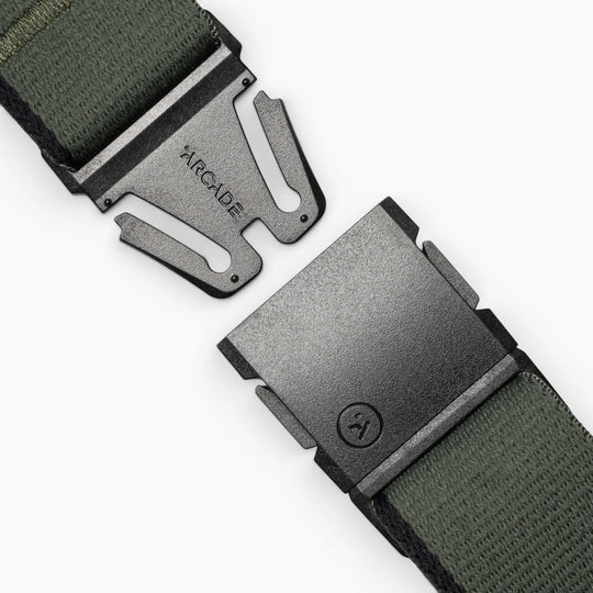 A close-up of a green Arcade Belts Blackwood fabric belt with a black metal A2 buckle, partially unclasped to reveal ARCADE engraved on the clasp.