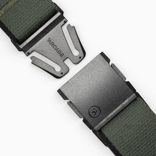 A close-up of a green Arcade Belts Blackwood fabric belt with a black metal A2 buckle, partially unclasped to reveal ARCADE engraved on the clasp.