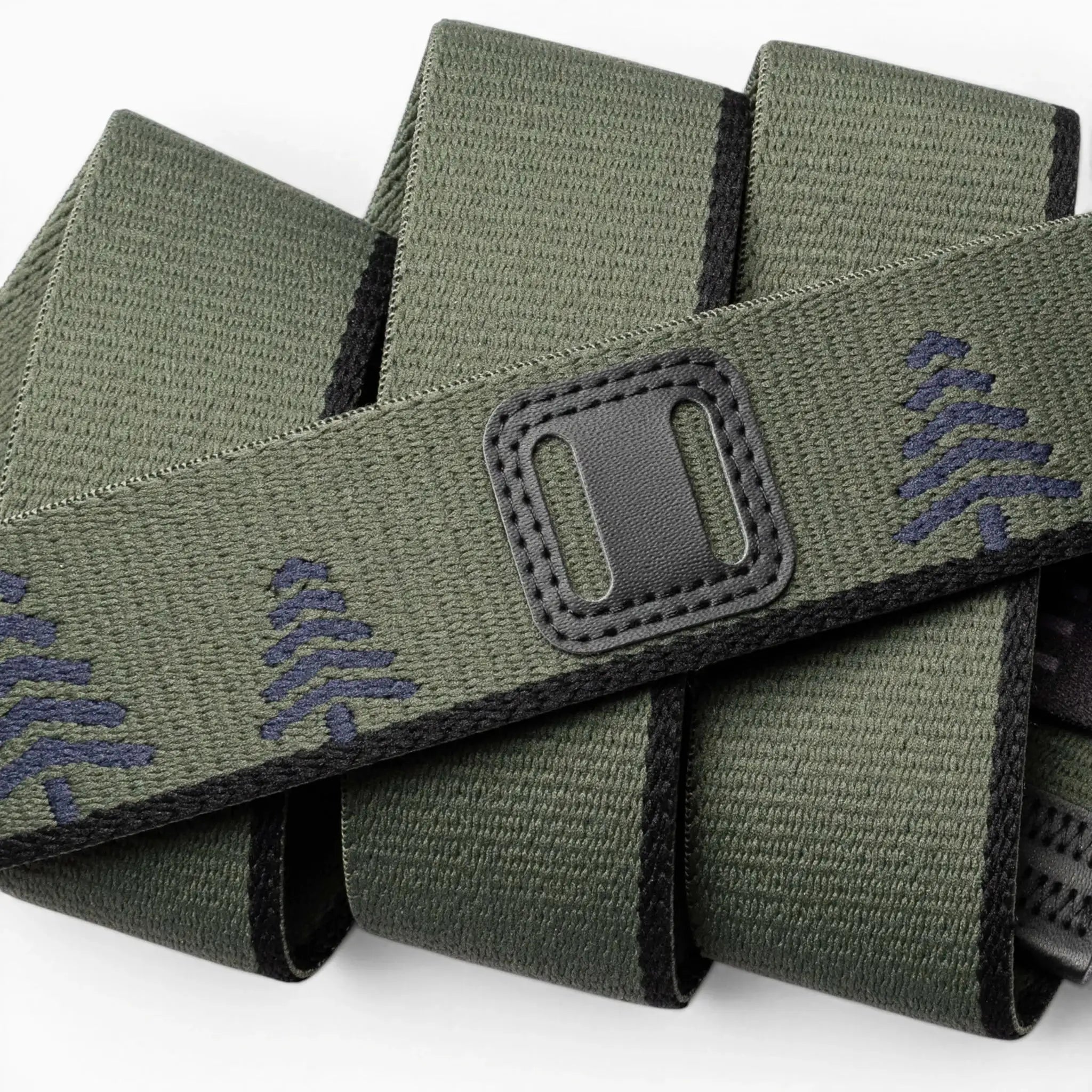 A close-up of the Blackwood belt by Arcade Belts: green fabric with black edging, decorated with navy blue tree patterns and a classic refreshed rectangular black patch featuring two horizontal openings.