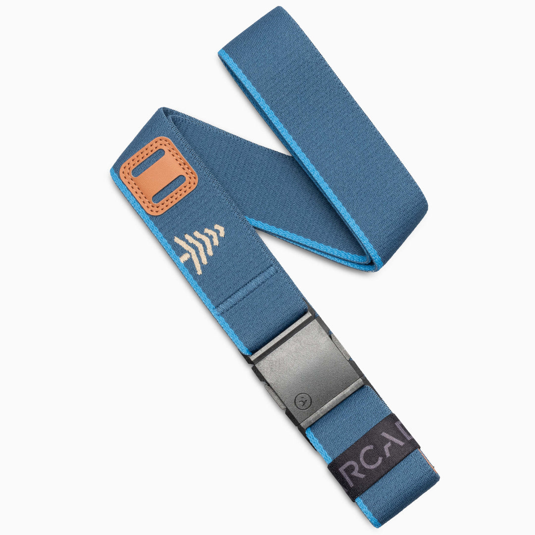 A Royal Sand elastic belt from Arcade Belts, featuring a metal A2 buckle, orange accent, and white arrow design. The end showcases a black label with partially visible “RCAN” text, reminiscent of an arcade classic. The Blackwood belt is displayed on a white background.