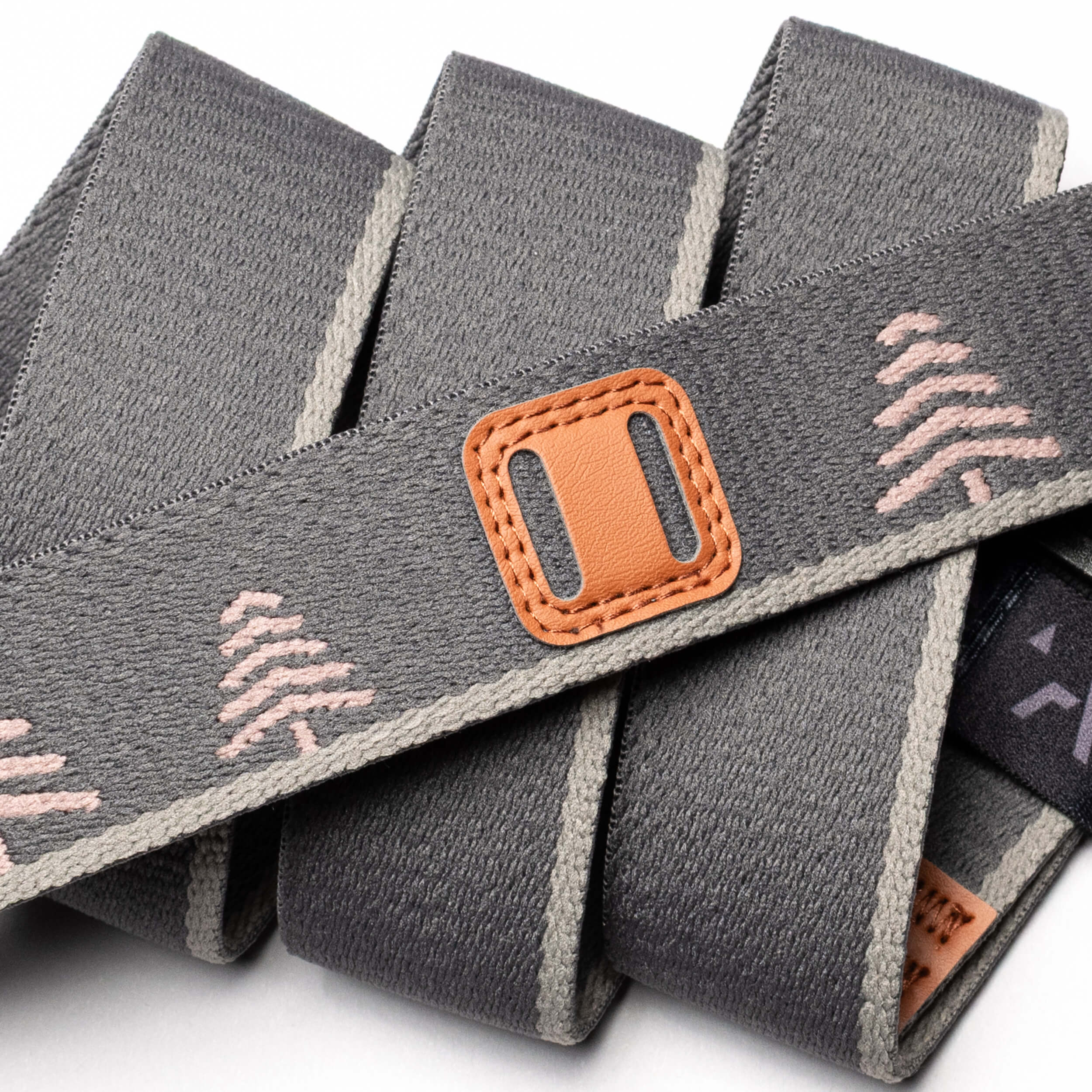 Close-up of the Blackwood strap by Arcade Belts: gray fabric with pink trees, beige edges, a brown stitched leather accent, neatly looped with a black tag and A2 buckle—ideal for stylish explorers.