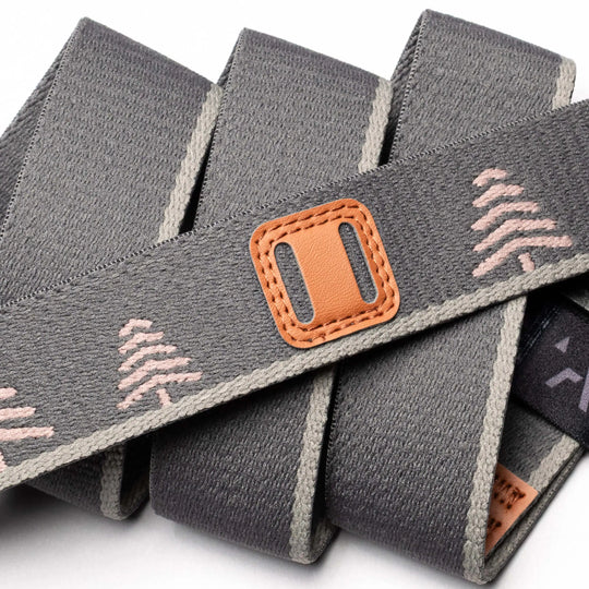 A close-up of the Arcade Belts Blackwood strap in gray, featuring light pink tree designs, beige edges, a stitched brown leather patch with rectangular slot, and an A2 buckle for a secure fit.